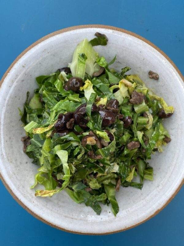 a bowl of spring greens topped with souri black olives