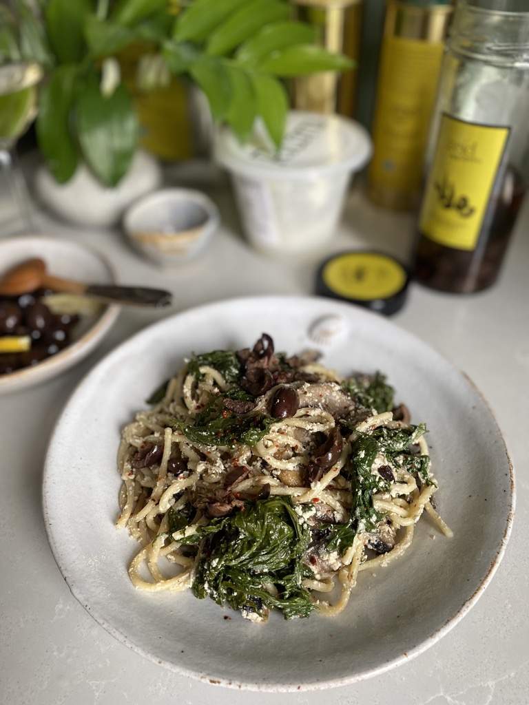 a plate with black souri olives on top of spaghetti kale and ricotta