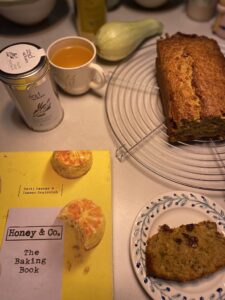 Honey & Co's The Baking Book with courgette cake and a cup of olive leaf infusion