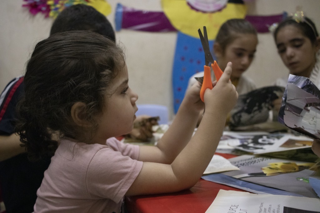 a girl with some orange scissors cutting up pictures in a classroom in Shatilla camp