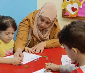 Nada with Rimas from Syria drawing a poster in a classroom