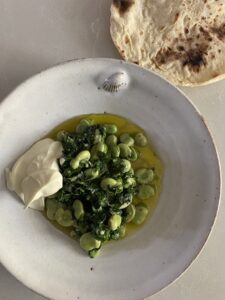 a plate of broad beans with coriander and garlic, a dollop of greek yoghurt and flat bread alongside served with extra virgin olive oil